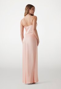 Abito lungo aderente in morbido satin rosa pallido. Presenta spalline sottili, una schiena bassa e un orlo fluido con dettagli di cucitura sottili.