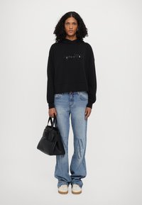 Black cropped hoodie with front logo detail, paired with blue wide-leg jeans featuring a subtle pattern, and a black handbag. White sneakers.