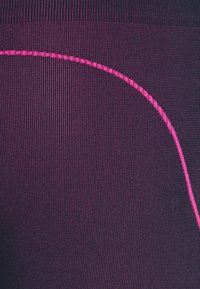 Lila sportiga leggings med en texturerad tyg, vertikal ribbning och en kontrasterande rosa söm som detalj längs sidan.