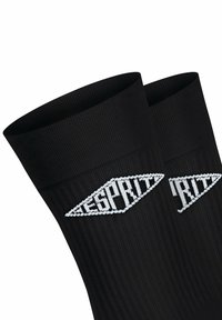 Schwarze gerippte Socken mit nahtlosem Design und einem weißen Logo in Diamantform. Das Material scheint gestrickt zu sein und bietet eine strukturierte Oberfläche.