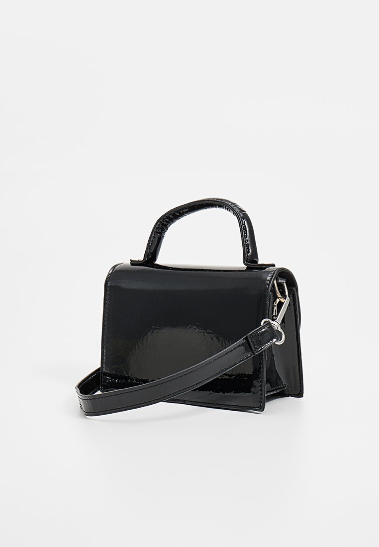 Sac à main en cuir verni noir avec une forme rectangulaire structurée, une courte poignée et une longue sangle détachable. Texture lisse et brillante.