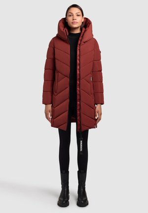 Rode pufferjas met een capuchon, met chevronstiksels, volledige rits aan de voorkant, zijzakken, gecombineerd met zwarte leggings en enkellaarsjes.