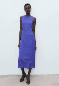 Sleeveless, mid-length dress in vibrant blue with black polka dots. Smooth fabric, fitted bodice, slight flare at the hem. Minimalist design.