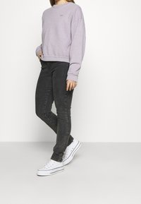 Felpa cropped viola chiaro con scollatura rotonda e dettagli con logo, abbinata a jeans skinny grigi scuri e sneakers bianche.