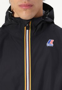 Black K-Way jacket featuring a front zipper with white, yellow, and red stripes, and an adjustable hood with toggle hardware.