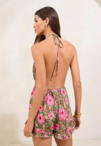 Mono corto floral con diseño sin espalda, flores rosas y verdes sobre un fondo de estampado de leopardo, tirantes ajustables al cuello y dobladillo con volantes.