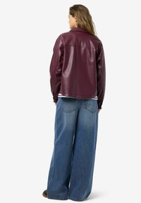 Bordeauxfarbene Kunstlederjacke mit lockerer Passform, ausgestattet mit gesenkten Schultern und einer glatten, glänzenden Oberfläche. Kombiniert mit weit geschnittenen Jeans.