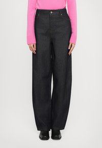 Bredde ben, mørke denimjeans med høy midje, med knappelukking og kontrasterende søm. Kombinert med en lys rosa genser.