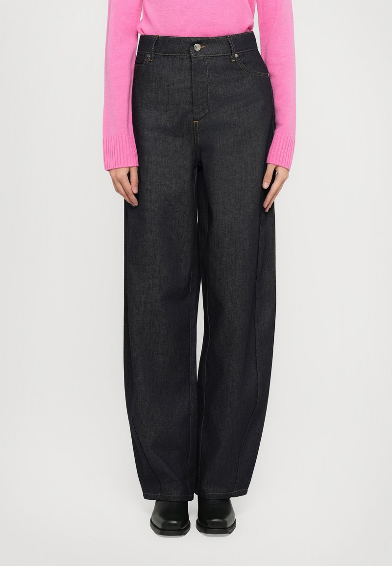Bredde ben, mørke denimjeans med høy midje, med knappelukking og kontrasterende søm. Kombinert med en lys rosa genser.