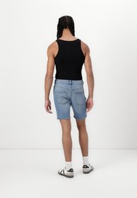 Șorturi din denim albastru cu margini destrămate, purtate cu un top negru și șosete albe, asortate cu pantofi negri și gri, văzute din spate.