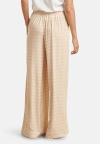 Leichte, lockere, beigefarbene Hosen mit einem weißen Chevron-Muster, ausgestattet mit einem elastischen Bund und weitem Bein. Weiches Stoffgefühl.
