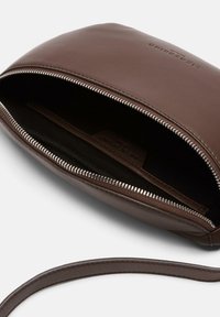 Clutch in pelle marrone con una texture liscia, chiusura a zip e un sottile cinturino da polso. Presenta una tasca interna e un dettaglio di branding.