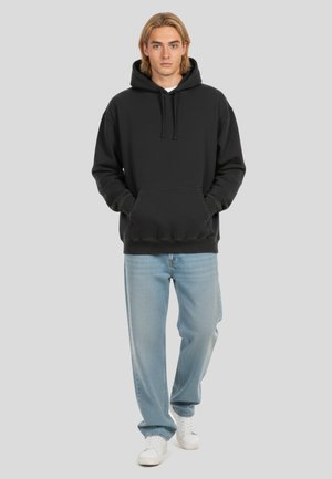 Felpa con cappuccio nera realizzata in materiale morbido, con tasca frontale; abbinata a jeans azzurri chiari e sneakers bianche. Design semplice e casual.