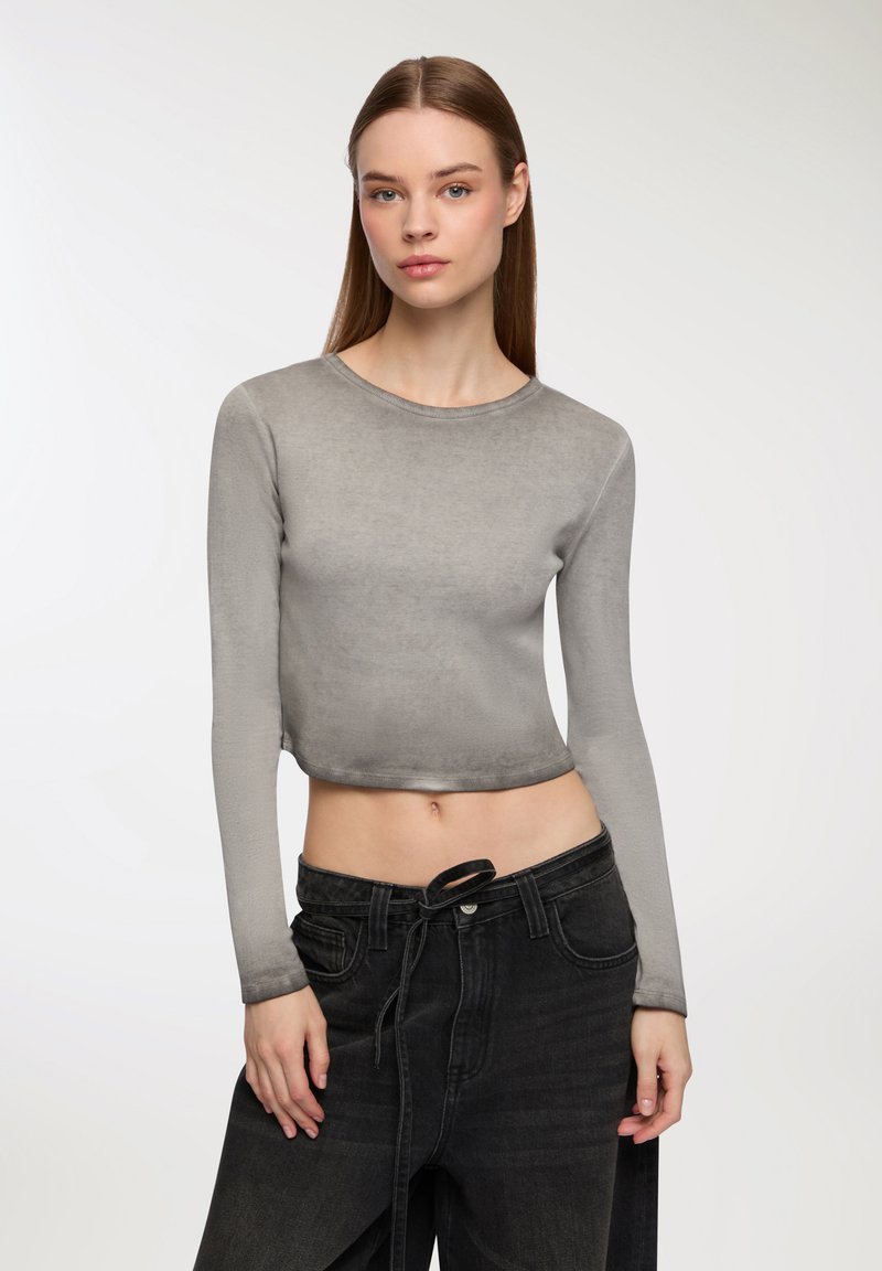 Szary, długi rękaw, krótki top o gładkiej teksturze. Połączony z czarnymi spodniami z wysokim stanem z regulowanym sznureczkiem. Prosty, nowoczesny design.