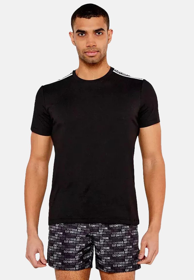 T-shirt noir à manches courtes avec un col rond, présentant des détails blancs sur les épaules. Associé à un short noir à motifs.