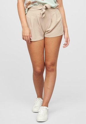 Pantaloni corti beige realizzati in un morbido tessuto testurizzato, dotati di un nodo anteriore, pieghe e una vestibilità rilassata, abbinati a sneakers bianche.