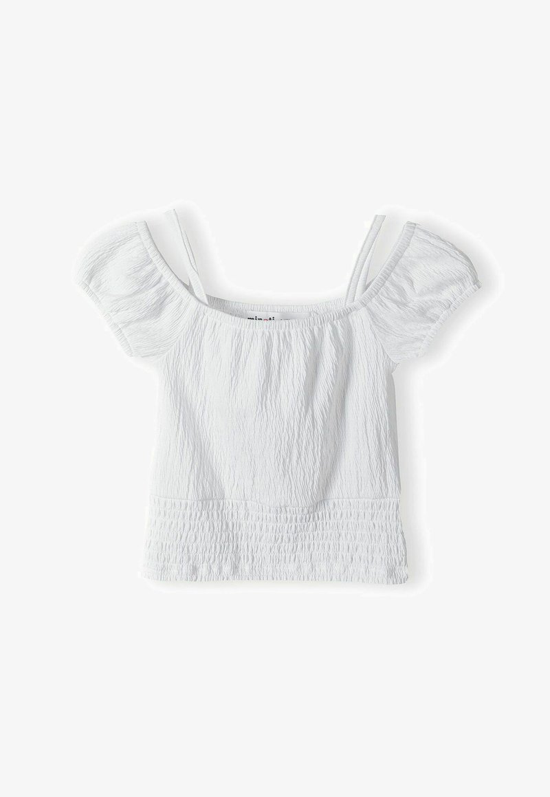 Balta topi bez plecu ar īsām pūkainām piedurknēm, teksturēta auduma, saplacināta viduklī un plāniem regulējamiem siksniņām, lai nodrošinātu pieguļošu izskatu.