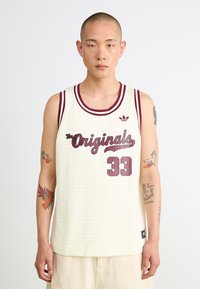 Bela mrežasta košarkarska majica z maroon poudarki, ki ima napis "The Originals" in številko "33." Logotip v zgornjem levem kotu.