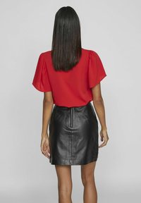 Czerwona bluzka krótki rękaw w stylu bufiastym, połączona z czarną skórzaną mini spódnicą z tylnym suwakiem. Gładka tekstura i dopasowany kształt.