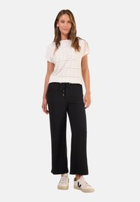 Chemise blanche avec un design découpé et des manches courtes, associée à un pantalon large noir et des baskets blanches avec des accents noirs.