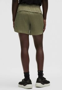 Zaļi, strukturēti šorti ar plašu, ručotu jostasvietu un izliekumu apakšmalā. Valkāti ar melnām sporta apaviem un tumšām zeķēm.