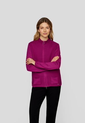 Fuchsia zip-up cardigan with a textured front, ribbed hem, and two front pockets, worn over black pants. Smooth knit fabric with stand collar.