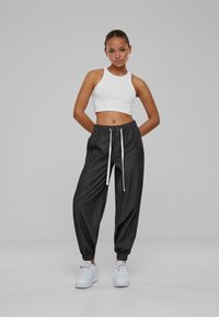 Black, loose-fitting joggers with white drawstring, paired with a white sleeveless crop top. Model wears white sneakers. Neutral background.