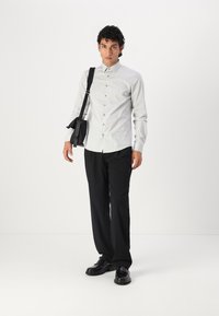 Lys grå skjorte med pointed krage, kombinert med svarte bukser og svarte sko. Personen bærer en svart crossbody-veske.