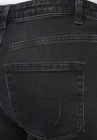 Jeans in denim nero con una tasca posteriore dotata di un discreto motivo cucito. Il materiale presenta una texture liscia con cuciture e dettagli visibili.