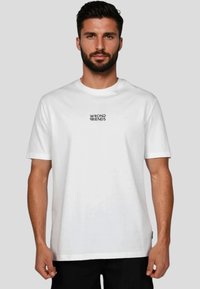 Hvid bomulds T-shirt med rund hals og korte ærmer, med "WRONG FRIENDS" trykt i sort på midten af brystet.