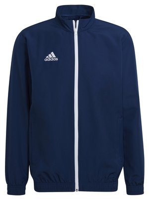 Giacca adidas blu navy, realizzata in tessuto morbido, presenta una cerniera bianca, colletto alto, polsini elasticizzati e tasche laterali. Design semplice.