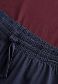 Bordowy materiał koszuli połączony z ciemnogranatowym pasem joggerów, wyposażony w marszczoną gumę i sznurek do regulacji.