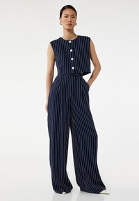 Ensemble coordonné marine comprenant un top cropped sans manches avec des rayures blanches et une panneau, ainsi que des pantalons larges avec des rayures verticales blanches.