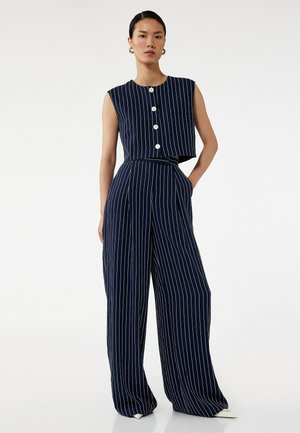 Laivastonsininen kaksiosainen asu, joka sisältää hihattoman lyhyen paidan, jossa on valkoiset raidat ja paneeli, sekä leveälahkeiset housut, joissa on pystysuorat valkoiset raidat.