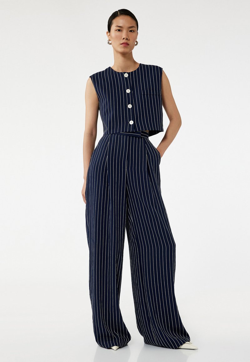 Ensemble coordonné marine comprenant un top cropped sans manches avec des rayures blanches et une panneau, ainsi que des pantalons larges avec des rayures verticales blanches.