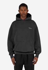 Czarna bawełniana bluza z kapturem, z troczkami, kieszenią z przodu, ściągaczami przy mankietach i u dołu. Ma subtelny, biały wyszywany logo na klatce piersiowej.