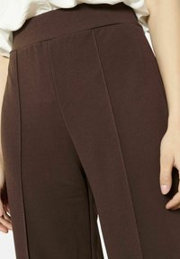 Pantalons larges marron avec une texture lisse, dotés d'une taille haute et de plis subtils pour une touche de détail.