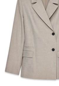 Beige kavaj med en strukturerad design, skarpa slag, dubbelknapplåsning och två platta fickor med horisontella sömmar.