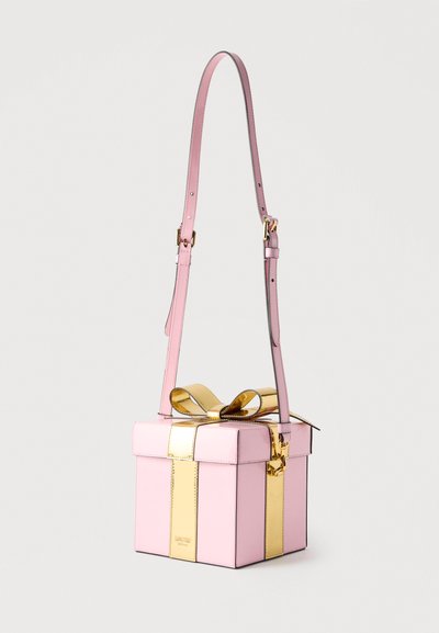 Ροζ τσάντα χειρός σε σχήμα κουτιού δώρου με λαμπερή χρυσή κορδέλα και ρυθμιζόμενο ιμάντα ώμου σε απλό φόντο.