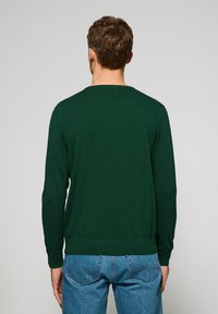 Mørkegrøn sweater med rund halsudskæring, ribbede manchetter og bund, samt en tætsiddende pasform, parret med lyseblå jeans.