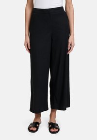 Zwarte wijde broek met een gladde textuur en een hoge tailleband, die is voorzien van discreet zijzakken en is gecombineerd met open-toed zwarte sandalen.