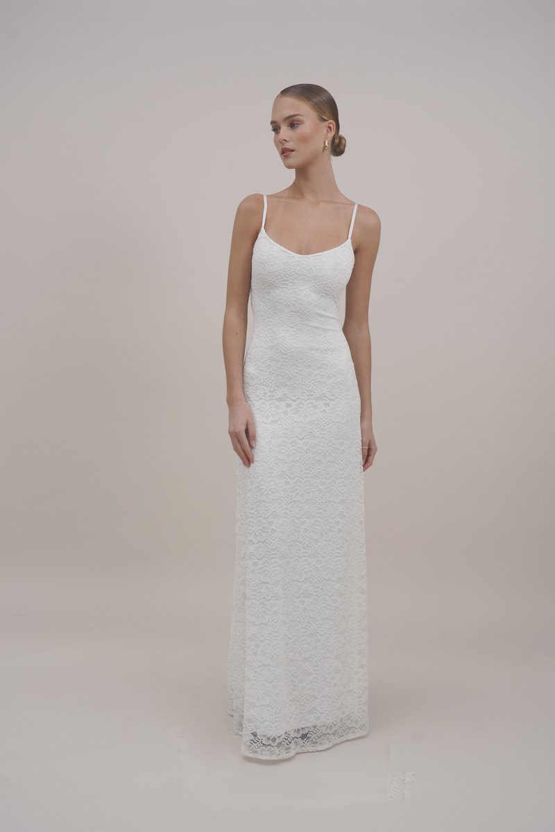 Rochie maxi albă din dantelă cu bretele subțiri, având un corset ajustat și un tiv evazat. Textura este detaliată cu modele florale de-a lungul întregii rochii.