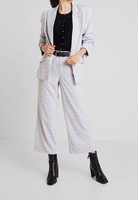 Grå ternet blazer med matchende bukser med vide ben, sort top, bælte i taljen og sorte ankelstøvler med hæl; glat stof, skræddersyet design.