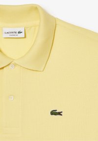 Polo Lacoste jaune, coupe classique, tissu texturé, trois boutons, col côtelé, avec logo crocodile vert brodé sur la poitrine.