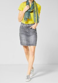 Grå denimkjol med framfickor, ljus blekning och en figurnära silhuett. Matchad med en gul skjorta och en teal scarf med svarta prickar.