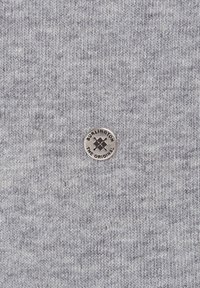 Tissu tricoté gris présentant un petit logo rond en métal avec le texte "BURLINGTON THE ORIGINAL" au centre. Apparence texturée et douce.