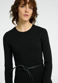 Robe en tricot noire à manches longues, col rond et une ceinture en cuir vert foncé contrastante nouée à la taille. Texture lisse.