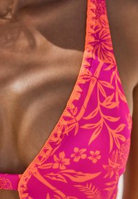 Rosa bikini med orange blommönster, med tunna band och strukturerad kant. Tyget verkar slätt och elastiskt.