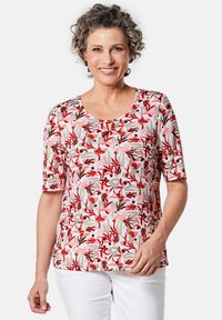 Korte mouwen top met een ronde halslijn, voorzien van een roze bloemenpatroon op een lichte achtergrond en een klein sleutelgaatje detail bij de nek.