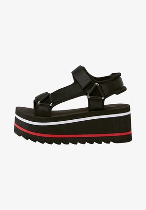 Sandalias de plataforma negras con correas anchas y hebillas ajustables. Rayas horizontales blancas y rojas adornan la suela gruesa. Patrón de banda de rodadura texturizado.